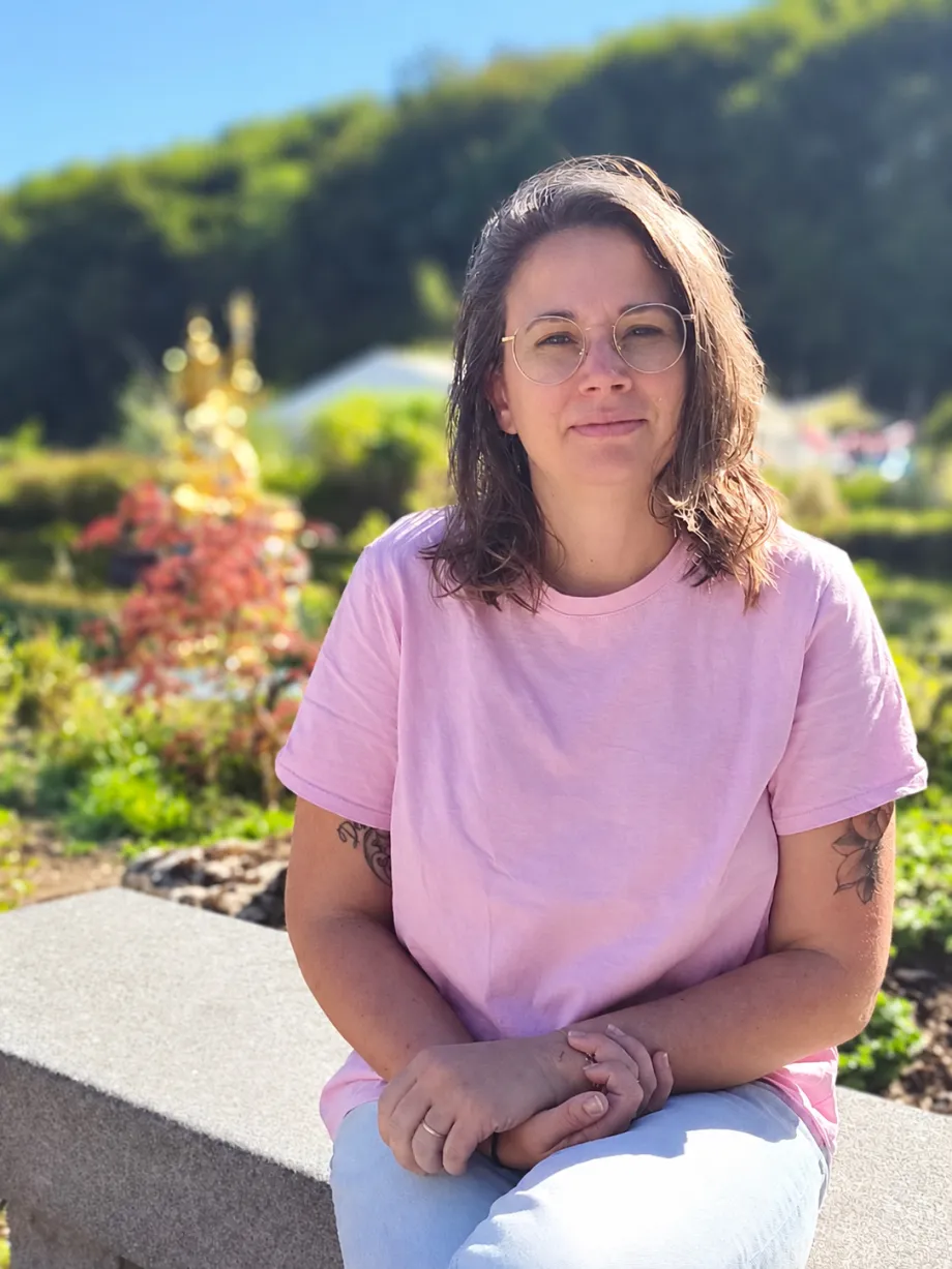 Lucille Dommartin, en t-shirt rose, assise sur un muret dans un jardin ensoleillé